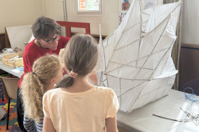 photo d'une animatrice qui montre une lanterne couverte de papier à deux jeunes filles - Agrandir l'image 8 sur 8, fenêtre modale