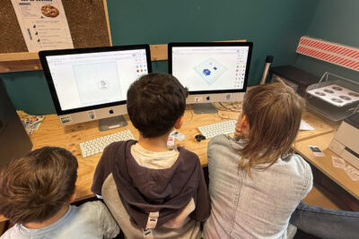 trois jeunes garçons sont assis devant deux macs en train de travailler sur un logiciel - Agrandir l'image 4 sur 8, fenêtre modale