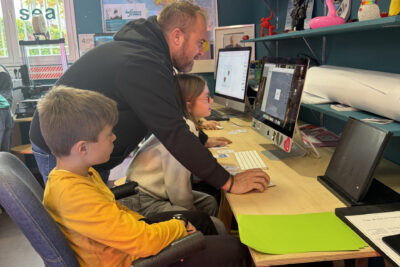photo de la pièce avec les ordinateurs, un animateur montre à une jeune fille quelque chose sur son ordinateur, un jeune garçon à côté regarde - Agrandir l'image 6 sur 8, fenêtre modale