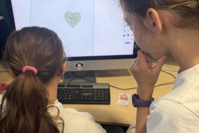 photo de deux jeunes filles qui travaillent sur une maquette en forme de coeur sur un logiciel à l'ordinateur, une est assise et l'autre debout à côté - Agrandir l'image 8 sur 8, fenêtre modale