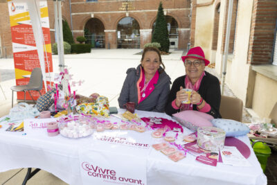 photo d'un stand associatif "vivre comme avant" avec deux femmes derrière le stand, assises qui sourient à l'objectif, sur la table, des friandises roses - Agrandir l'image 12 sur 21, fenêtre modale