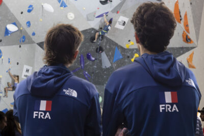 photo de deux athlètes pris de dos, on les voit regarder, debout et bras croisés, le mur avec quelqu'un qui grimpe - Agrandir l'image 55 sur 68, fenêtre modale