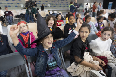 photo d'un groupe d'enfants qui encouragent les grimpeurs, au premier plan une jeune fille déguisée en sorcière avec un chapeau pointu - Agrandir l'image 57 sur 68, fenêtre modale