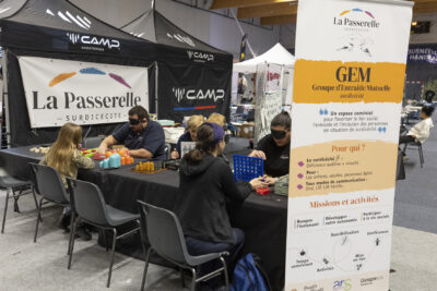 photo du stand de la Passerelle, association d'entraide pour les personnes déficientes auditives et visuelles, des personnes jouent à des jeux de société à table - Agrandir l'image 13 sur 68, fenêtre modale