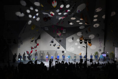 photo de la finale, les grimpeurs en ligne devant le mur éclairés tandis que le public devant est dans l'ombre - Agrandir l'image 15 sur 68, fenêtre modale