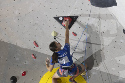 photo d'une grimpeuse qui tient une prise d'une main et s'apprête à aller sur une autre - Agrandir l'image 20 sur 68, fenêtre modale