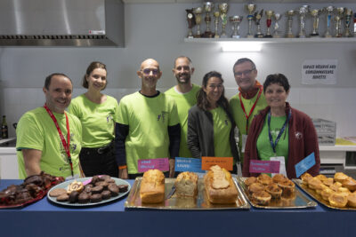 photo de bénévoles en teeshirt vert clair derrière un stand de nourriture (gâteaux sucrés) - Agrandir l'image 32 sur 68, fenêtre modale