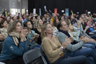 photo du public qui applaudit dans la salle, assis sur des chaises - Agrandir l'image 38 sur 68, fenêtre modale