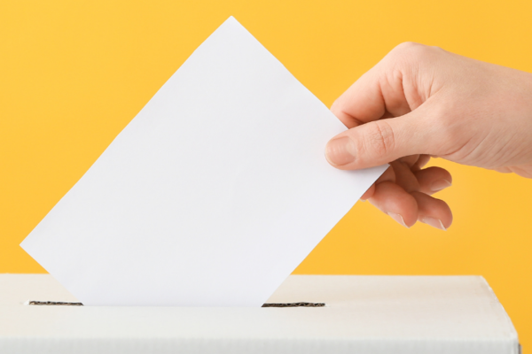 photo coupée avec juste main qui dépose un bulletin de vote dans une urne, sur un fond jaune