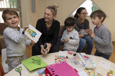 photo de trois enfants et deux femmes près d'une table, un enfant montre son dessin de personnage de minion et sourit à l'objectif - Agrandir l'image 11 sur 32, fenêtre modale