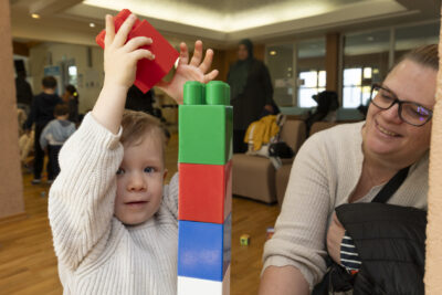 un enfant avec une femme, l'enfant s'apprête à poser une pièce de légo sur une tour faite en légo - Agrandir l'image 10 sur 32, fenêtre modale