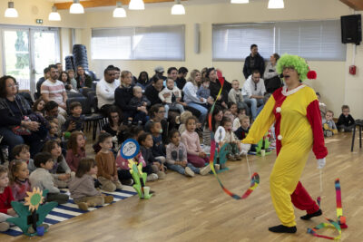 photo d('un clown qui fait un spectacle avec des rubans colorés face à de nombreux enfants rassemblés dans une salle - Agrandir l'image 1 sur 32, fenêtre modale