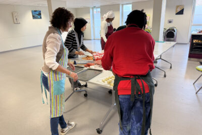 photo d'un atelier cuisine, quatre femmes sont rassemblées debout autour d'une table qu'elles utilisent comme un plan de travail - Agrandir l'image 28 sur 32, fenêtre modale