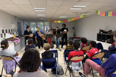 photo d'un petit concert dans une salle d'école, avec des enfants assis qui regardent des musiciens - Agrandir l'image 27 sur 32, fenêtre modale
