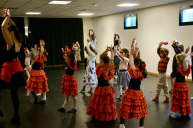 photo du groupe d'enfants dans la salle, une quinzaine, qui dansent les mains en l'air et croisées dans une salle