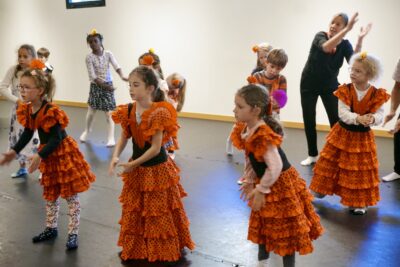 photo de jeunes enfants qui dansent, au premier plan trois jeunes fille sen robe orangée, les mains devant elles en cercle - Agrandir l'image 2 sur 7, fenêtre modale