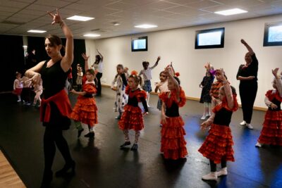 le groupe d'enfants s'entraîne à danser comme l'adulte devant, une main en haut et l'autre au niveau de la poitrine, comme avec le flamenco - Agrandir l'image 4 sur 7, fenêtre modale