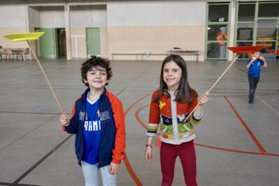 deux enfants sourient à l'objectif en tenant chacun un baton en bois surmonté d'une sorte d'assiette en équilibre - Agrandir l'image 15 sur 16, fenêtre modale