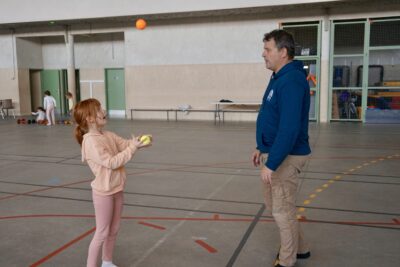 une jeune fille jongle avec deux balles devant un homme dans un gymnase - Agrandir l'image 12 sur 16, fenêtre modale