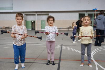trois enfants debout dans un gymnase tiennent ce qui ressemble à un bâton de majorette en équilibre grâce à deux autres batons - Agrandir l'image 9 sur 16, fenêtre modale