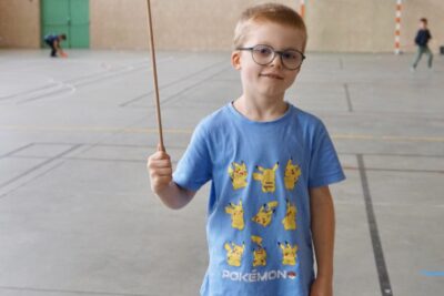photo d'un jeune garçon dans un gymnase qui fait tourner une assiette en plastique orange en équilibre sur un piquet en bois - Agrandir l'image 3 sur 16, fenêtre modale