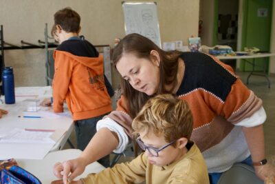 une femme montre à un jeune garçon quelque chose sur sa feuille sur laquelle il a dessiné - Agrandir l'image 3 sur 10, fenêtre modale