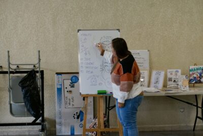 une femme montre des dessins sur un support avec des grandes feuilles blanches - Agrandir l'image 8 sur 10, fenêtre modale