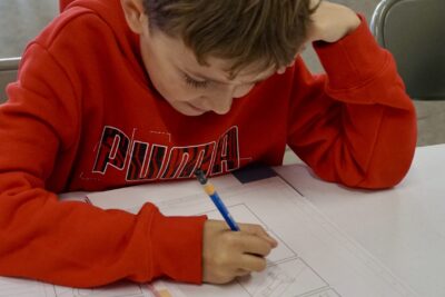 un jeune garçon avec un swear puma rouge dessine sur une feuille blanche avec des cases - Agrandir l'image 9 sur 10, fenêtre modale
