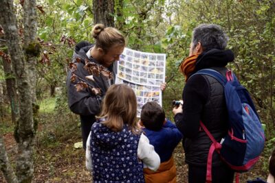 photo d'un homme qui montre des photos d'insectes à deux enfants, sous les arbres - Agrandir l'image 2 sur 14, fenêtre modale