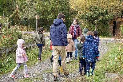 photo du groupe d'une dizaine d'enfants qui marchent avec deux adultes dans une allée dans les jardins partagés - Agrandir l'image 3 sur 14, fenêtre modale
