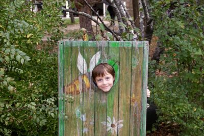 un enfant a sa tête dans un trou dans un assemblage de planches peintes, il sourit pour la photo - Agrandir l'image 11 sur 14, fenêtre modale