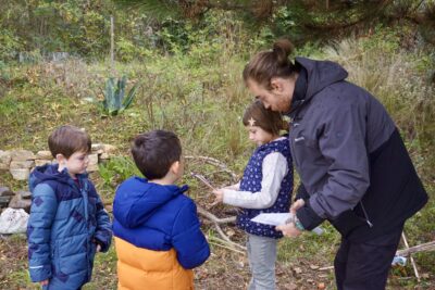 Un homme explique à trois enfants quelque chose, dans la nature, tous sont habillés assez chaudement et pour la pluie - Agrandir l'image 14 sur 14, fenêtre modale