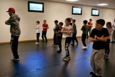 photo d'une dizaine d'enfants debout dans une salle de danse qui imitent l'animateur, bras croisés - Agrandir l'image 3 sur 9, fenêtre modale