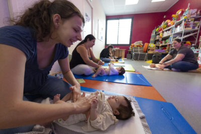 photo d'un atelier massage bébé, au premier plan une femme masse le vendre d'un bébé allongé sur un tapis - Agrandir l'image 23 sur 32, fenêtre modale