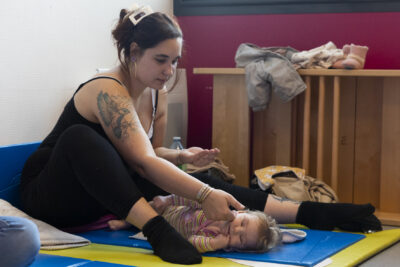 photo d'une femme avec son bébé, le bébé est allongé sur un petit tapis et elle est assise devant lui, elle caresse sa joue - Agrandir l'image 25 sur 32, fenêtre modale