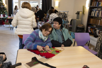 photo de deux femmes âgées assises à table, une découpe un tissu coloré - Agrandir l'image 23 sur 26, fenêtre modale