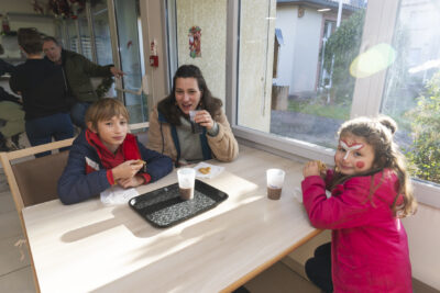 photo de deux enfants et d'une femme assis à une table, ils ont un chocolat chaud et mangent une crêpe, un des enfants est maquillé - Agrandir l'image 2 sur 26, fenêtre modale