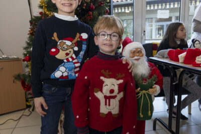 deux enfants posent devant un sapin de Noël, tout sourires, ils portent des lunettes rondes et des pulls de Noël - Agrandir l'image 5 sur 26, fenêtre modale
