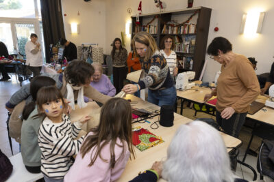 photo de femmes de toutes générations assises à table, dans une salle, d'autres femmes autour regardent - Agrandir l'image 12 sur 26, fenêtre modale