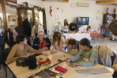 photo d'un groupe de trois jeunes filles, deux femmes âgées assises à table en train de préparer des paquets cadeaux