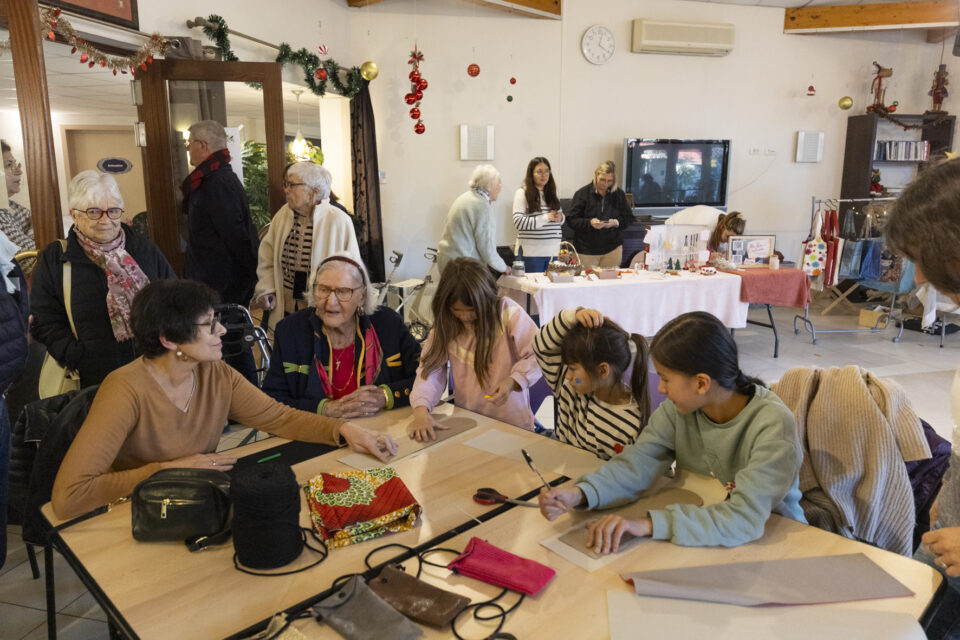 photo d'un groupe de trois jeunes filles, deux femmes âgées assises à table en train de préparer des paquets cadeaux