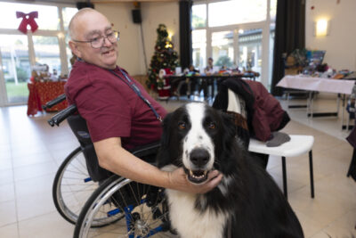 photo d'un homme dans un fauteuil roulant avec son chien noir et blanc qui regarde vers l'objectif - Agrandir l'image 13 sur 26, fenêtre modale