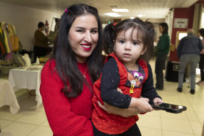 une femme tient une petite fille dans ses bras, les deux sont brunes et habillées en rouge, elles sourient à l'objectif - Agrandir l'image 7 sur 26, fenêtre modale