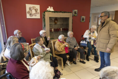 photo du Maire qui échange avec une dizaine de personnes âgées assises en train de manger une crêpe en souriant - Agrandir l'image 20 sur 26, fenêtre modale
