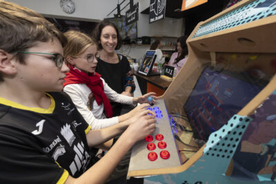 une jeune fille et un jeune garçon jouent à une borne d'arcade pendant qu'une femme les regarde - Agrandir l'image 16 sur 32, fenêtre modale