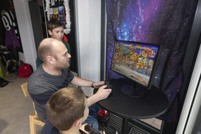 un homme et deux jeunes garçons jouent à un jeu rétro dans une pièce - Agrandir l'image 19 sur 32, fenêtre modale