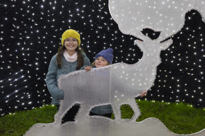 deux enfants se tiennent debout derrière une illumination en forme de renne blanc et sourient à l'objectif - Agrandir l'image 4 sur 20, fenêtre modale