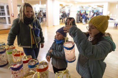une jeune fille prend un lampion éclairé dans une salle, à côté d'elle une petite fille et une femme adulte tout sourire - Agrandir l'image 19 sur 20, fenêtre modale