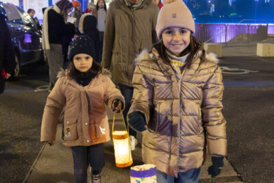 photo de jeunes filles qui marchent avec leurs lampions, derrière on voit la façade de l'Escale bleue et éclairée - Agrandir l'image 14 sur 20, fenêtre modale