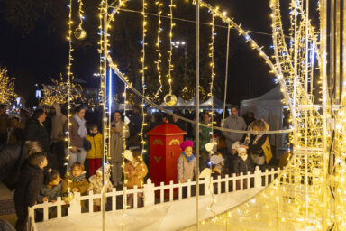 des enfants sont rassemblés devant l'illumination sur le parvis de la mairie, on voit des familles derrière dans la nuit